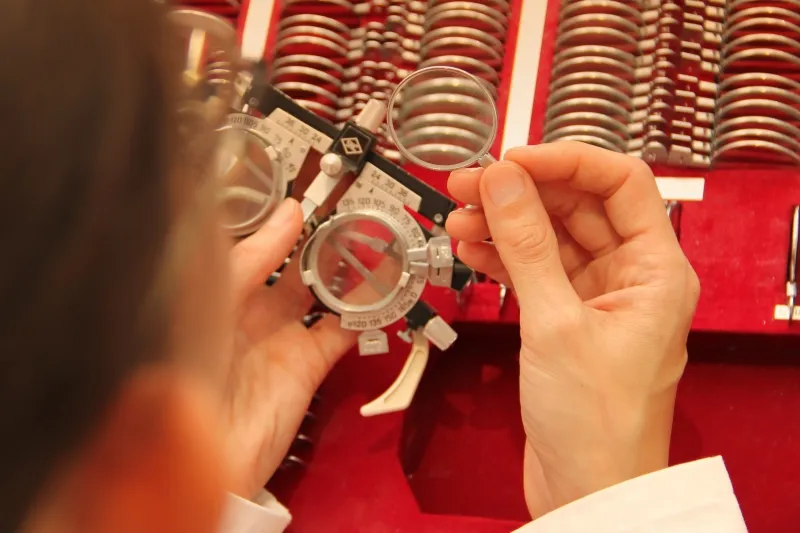 Hands holding a trial lens frame in front of a case of trial lenses